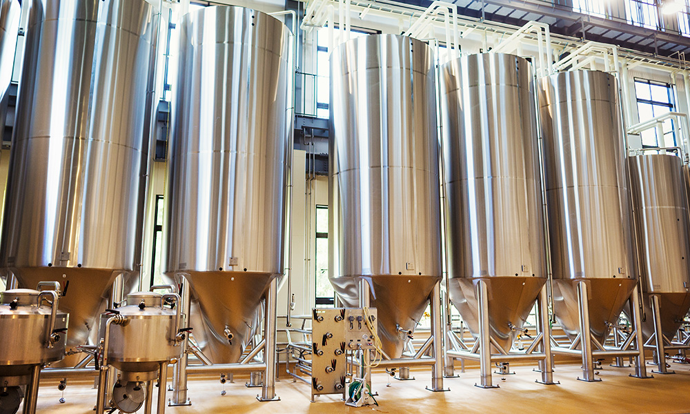 A photograph of a row of stainless steel brewery fermenters in bright daytime.